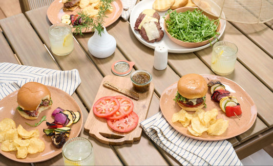 A summer picnic spread with burgers, potato chips, tomatoes, grilled skewers, and more. 