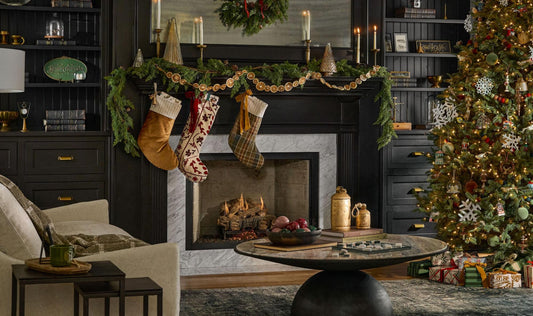 Living room decorated for Christmas. Stockings hang on a mantel above the fireplace and a Christmas tree is seen to the side.