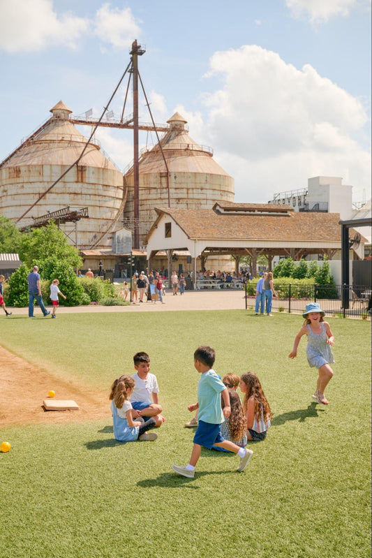 Children run around a green lawn at the Magnolia Silos in Waco, Texas.