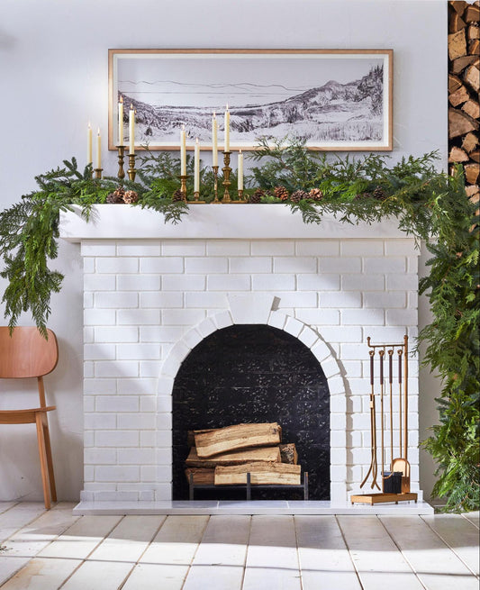 white painted brick fireplace with green garland, tapers and taper holders and a horizontal landscaped framed picture hung above the mantel.