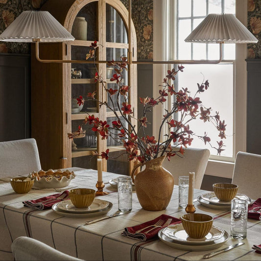 A unique chandelier hung above a long dining table set with neutral tableware and a vase of faux florals.