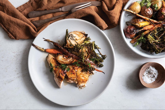 A plate of chicken and roasted, mixed vegetables with antique flatware