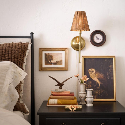 a decorated nightstand with books, framed art. bud vases, and a wall sconce.