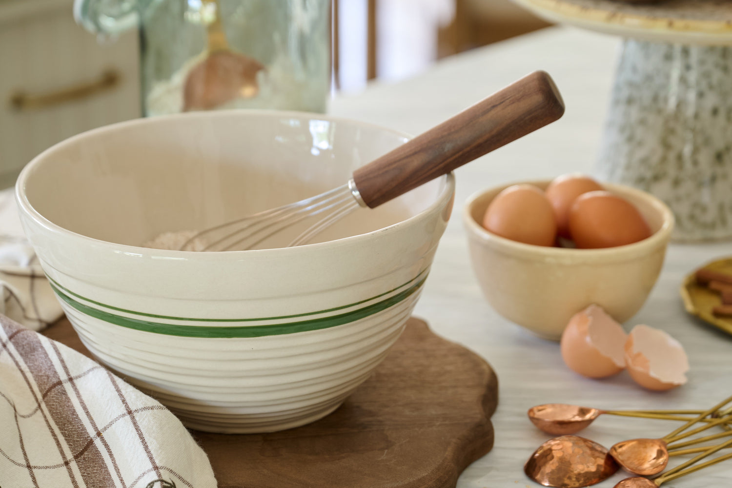 Shop mixing bowls. Image features an ivory mixing bowl with a wooden whisk to stir.