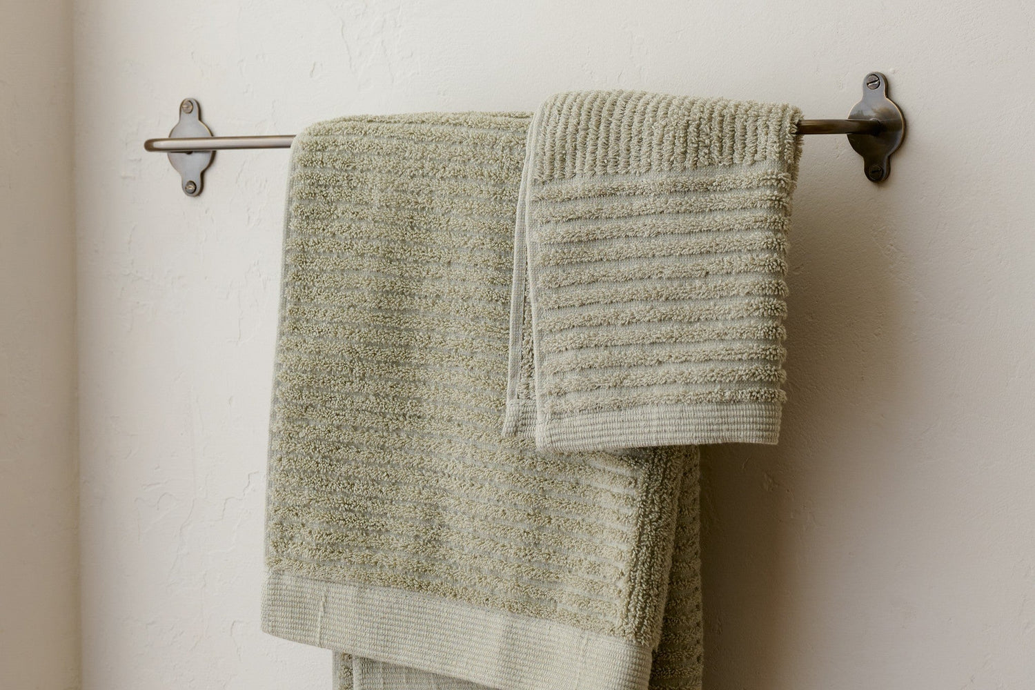 Shop bathroom towels and bath mats. Image features green bath towels hanging on towel rack.