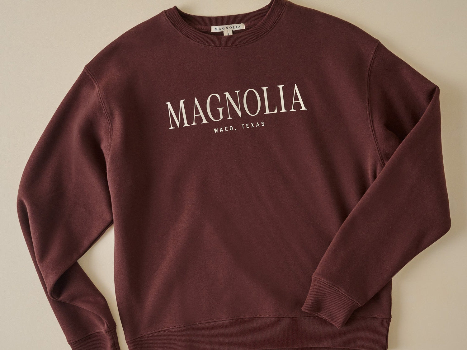 shop magnolia clothing. Image features burgundy crewneck sweatshirt reads magnolia waco, texas