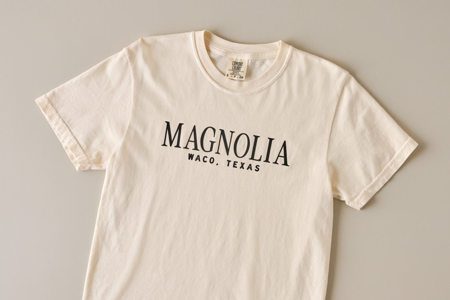 Shop t-shirts. Image features short sleeve ivory tee with magnolia on front.