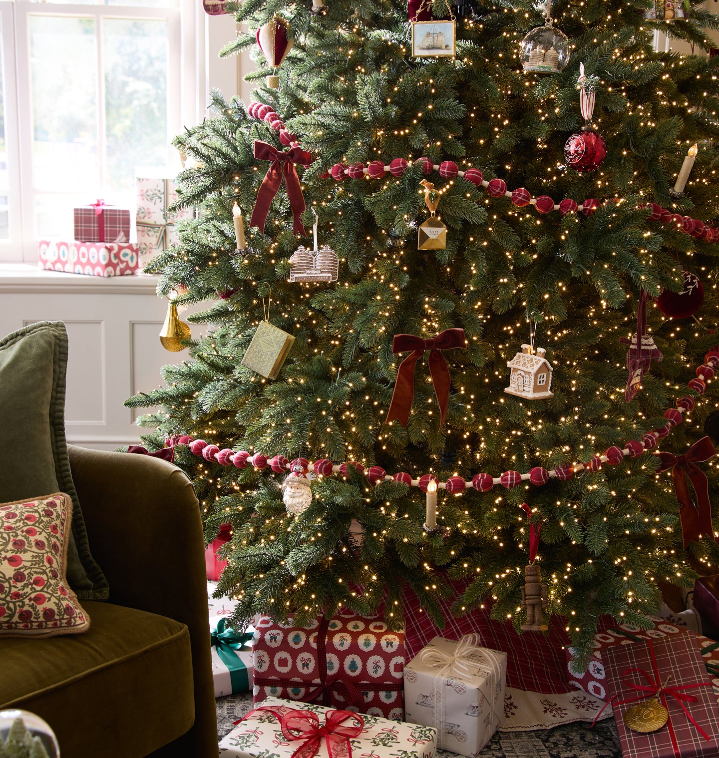 Decorated Christmas tree with lights, ornaments, and presents in a living room.