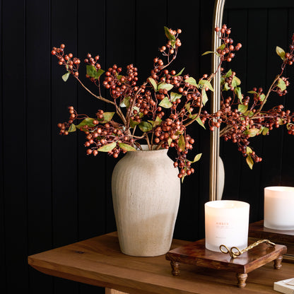 Brown Berry Spray with Green Leaves in a vase on a table next to a candle