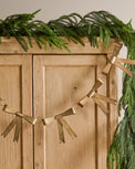Gloria Brass Bow Garland shown hung on furniture with other greenery