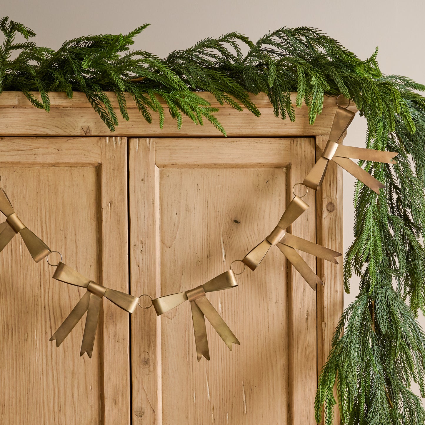 Gloria Brass Bow Garland shown hung on furniture with other greenery
