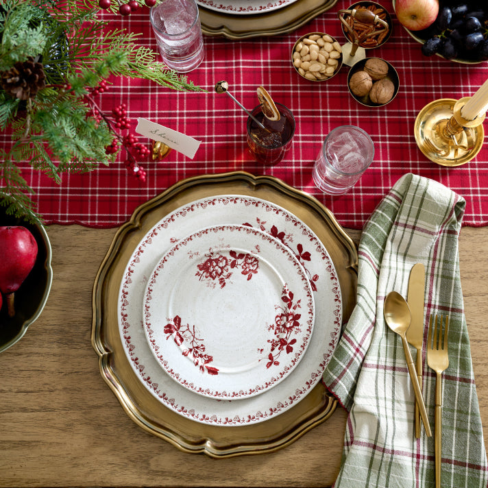 Christmas table setting with red plaid tablecloth, gold charger plate, and decorative plates.