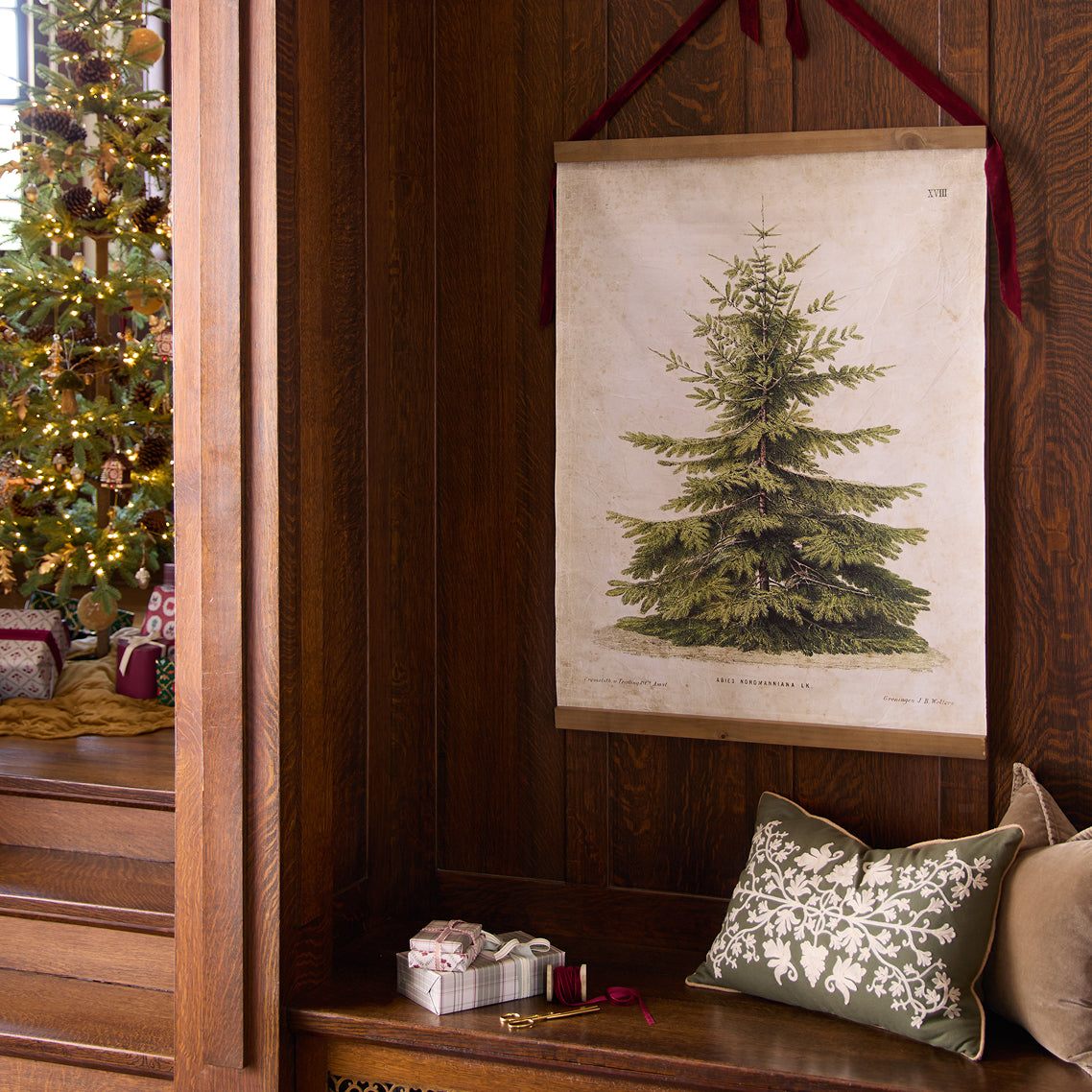 Decorative Christmas scene with a printed tree on a wall, pillows, and a Christmas tree in the background.