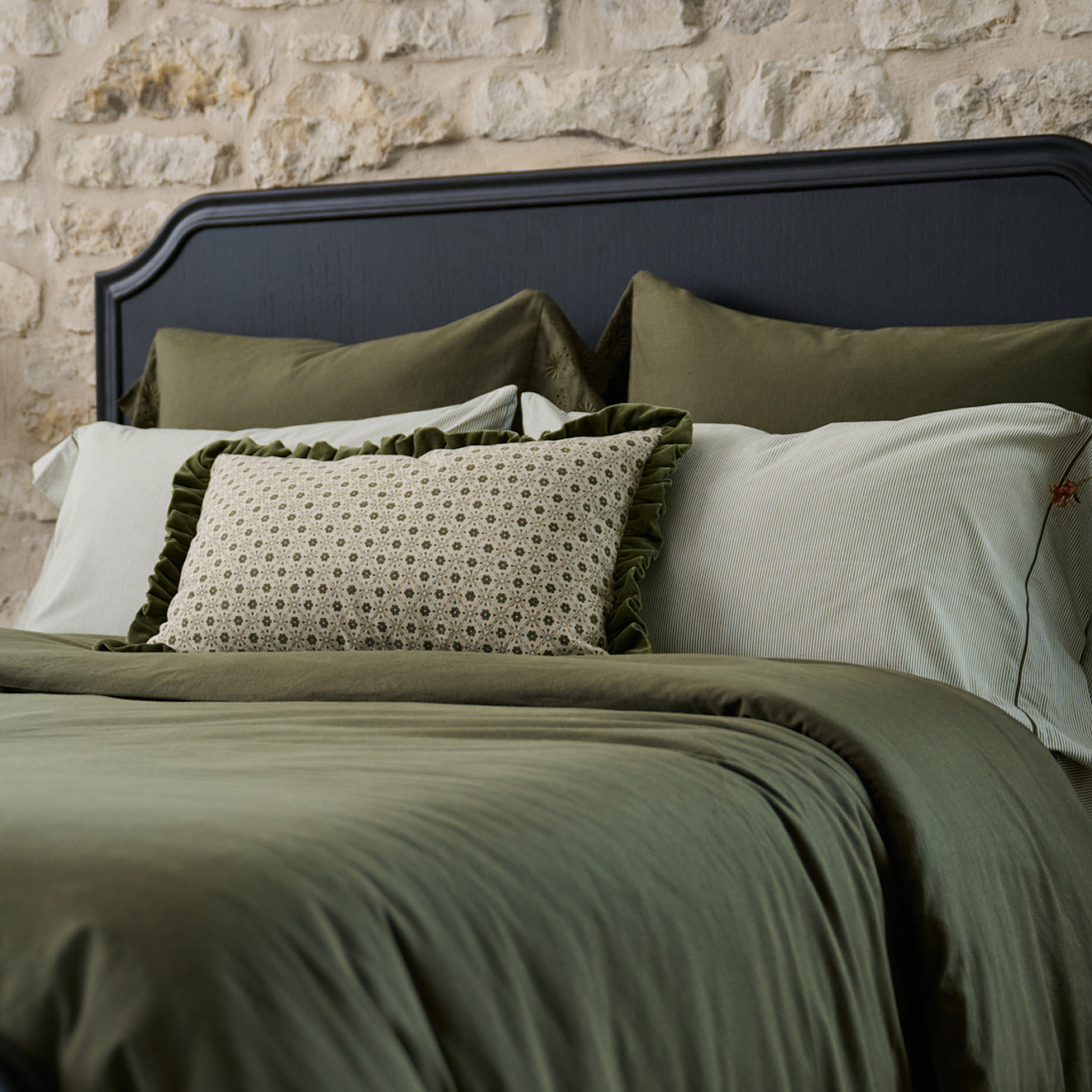 Bed with green bedding and pillows against a stone wall