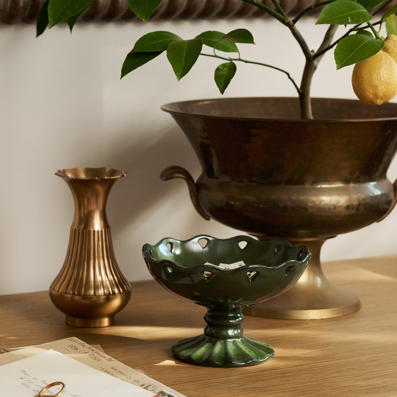 Decorative items including a brass vase, green ceramic bowl, and bronze urn on a wooden surface.