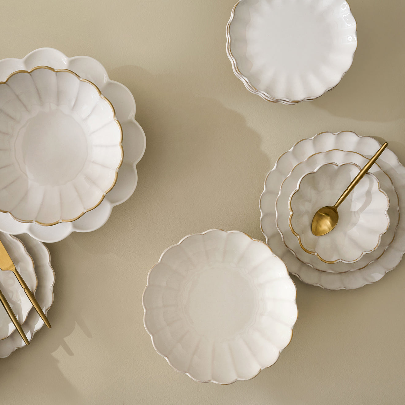 Set of white ceramic scalloped plates with gold accents on a beige background.