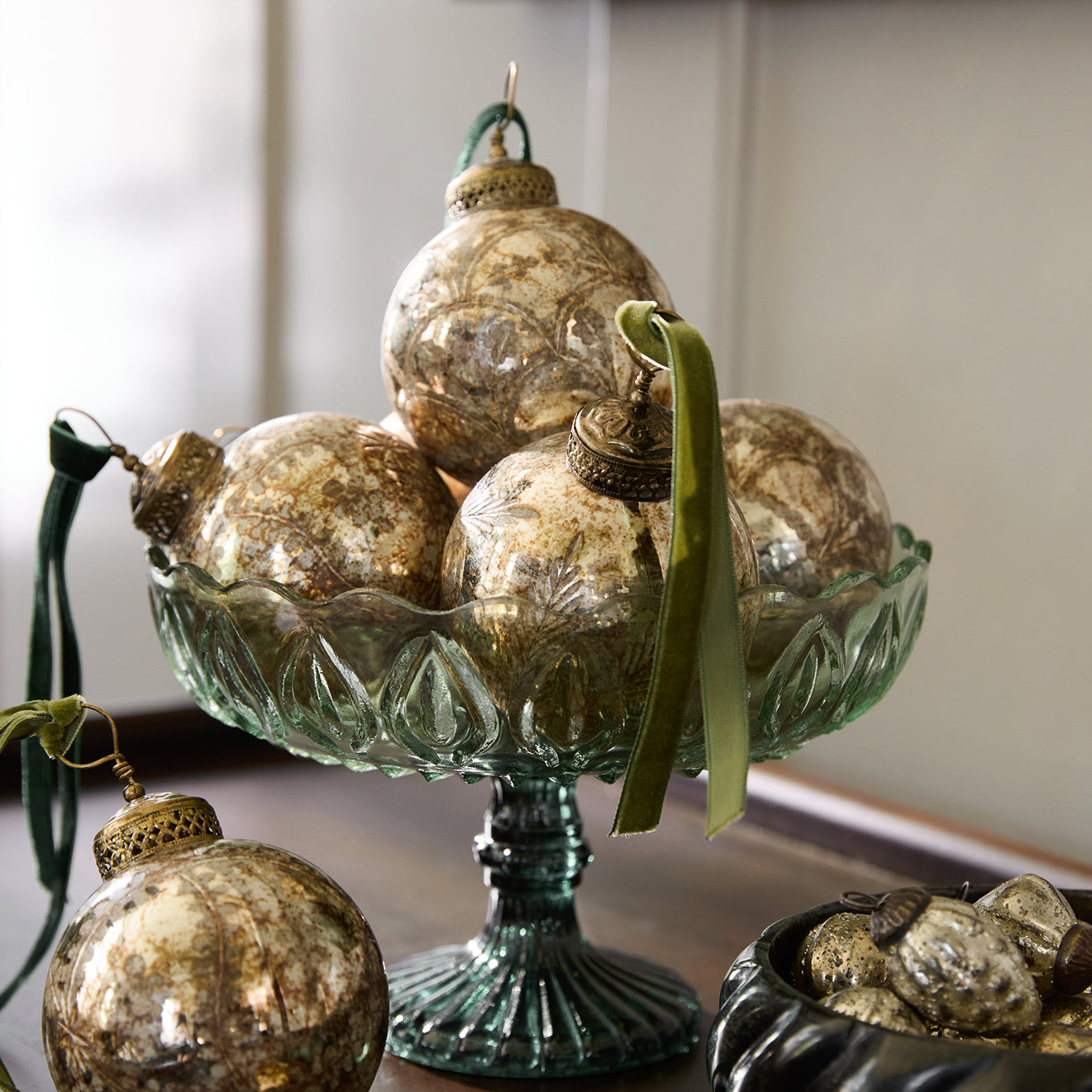 Decorative glass ornaments in a green decorative glass bowl on a wooden tabletop.