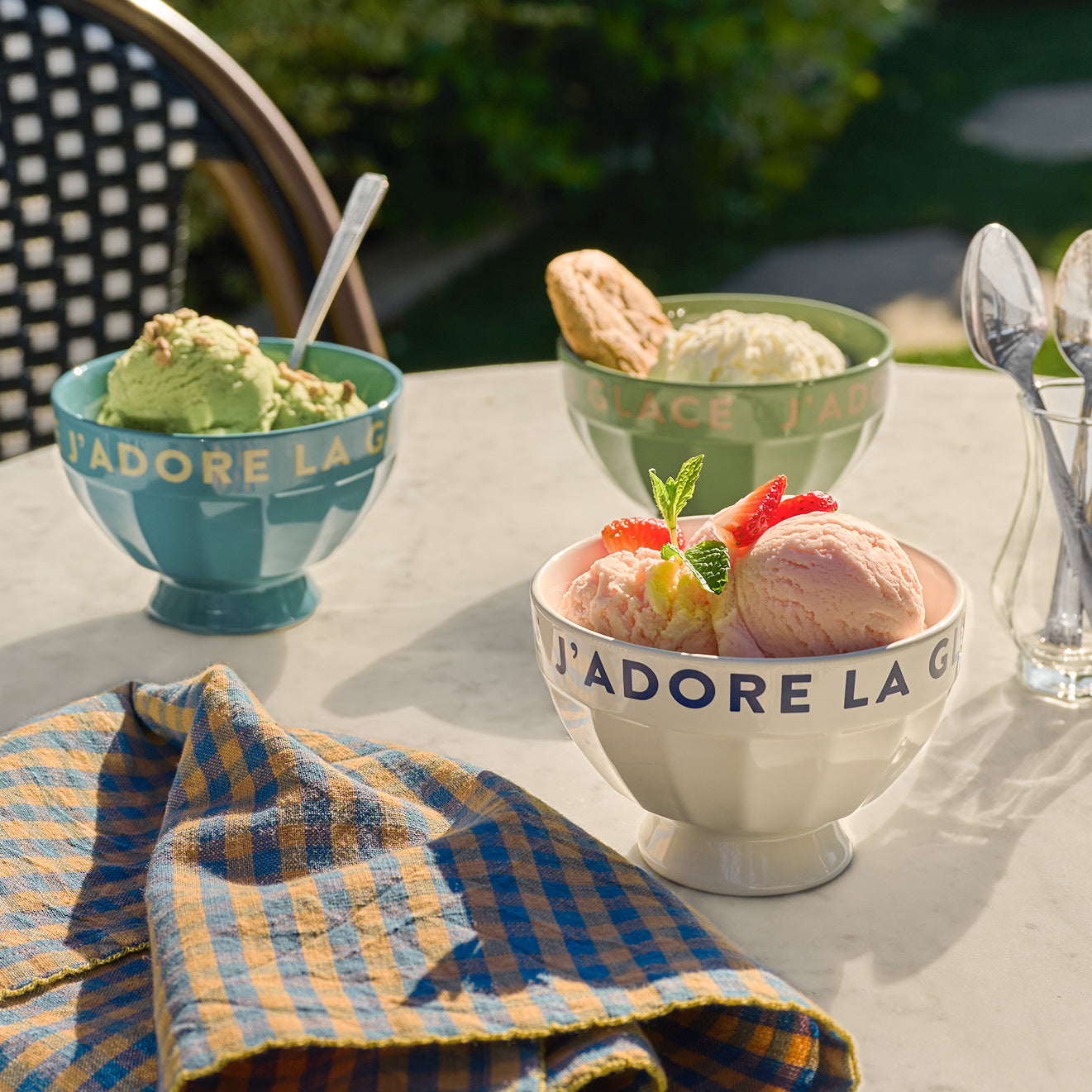 Three bowls of ice cream with spoons on a table outdoors.