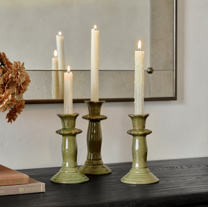 Three green ceramic candle holders with lit candles on a wooden surface.