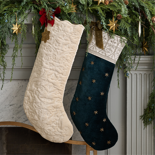 Two Christmas stockings, one white and one dark blue with gold stars, hanging on a fireplace mantel.