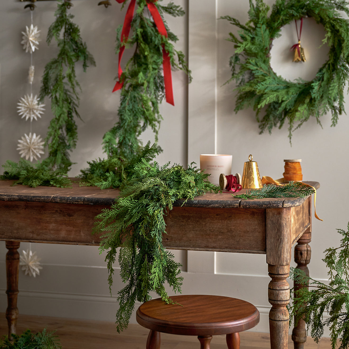 Decorative Christmas setting with greenery, a candle, and a bell on a wooden table.