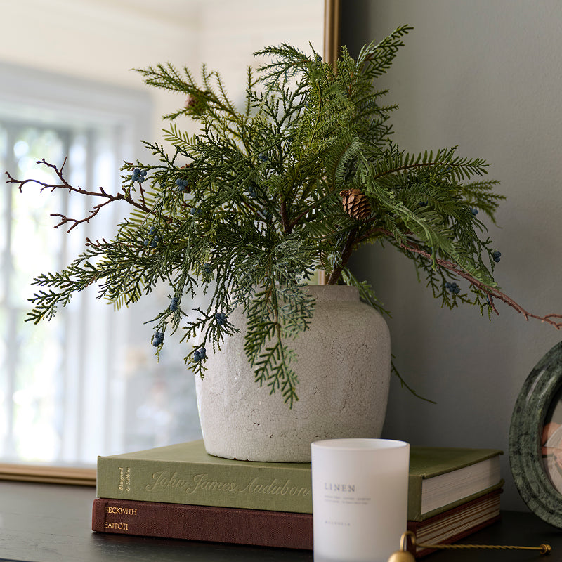 faux greenery in a crackled white vase sitting on top of books with a linen candle in front.