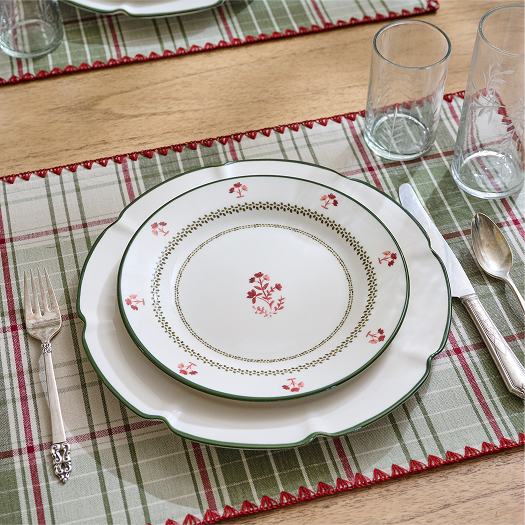 Set table with decorative plate, cutlery, and glasses on a plaid placemat.