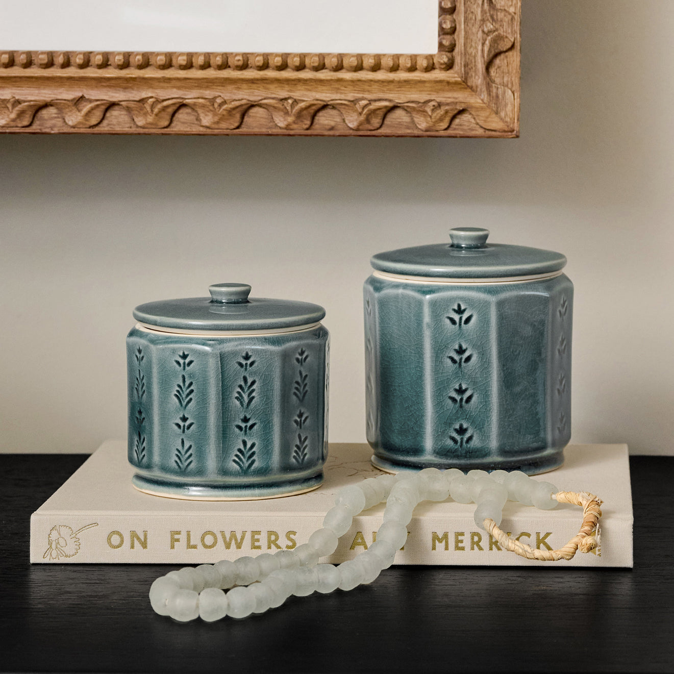 Two blue ceramic jars with decorative patterns on a book against a neutral wall.
