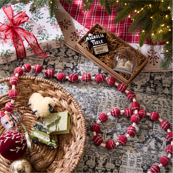 Decorative Christmas scene with red and white bead garland, basket of ornaments, and gift box under a tree.
