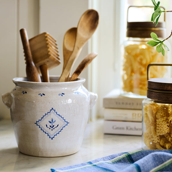 White ceramic jar with blue decorative pattern containing wooden utensils on a kitchen counter.