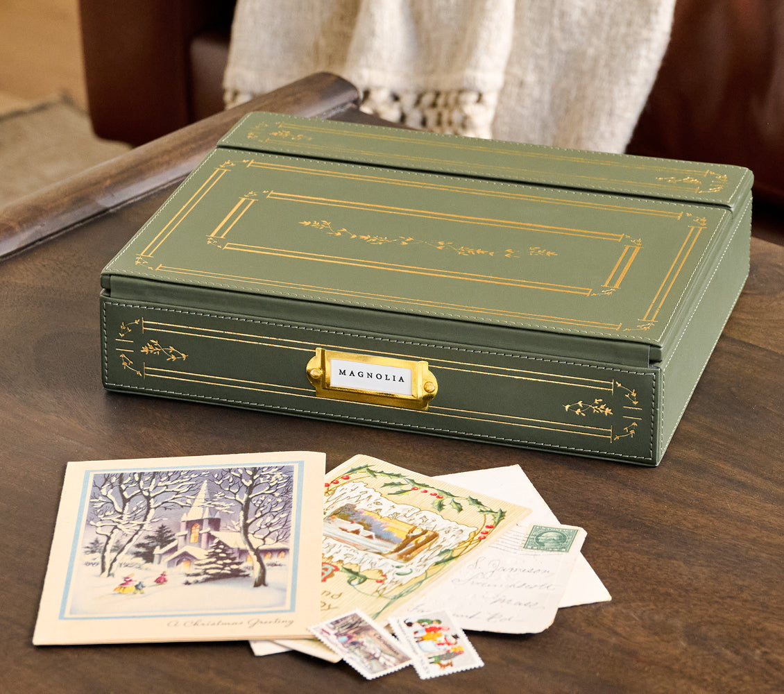 Green leather box with 'Magnolia' branding on a wooden surface with vintage cards.