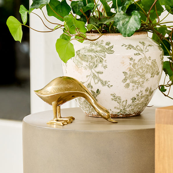 Gold bird figurine next to a decorative plant pot with floral patterns