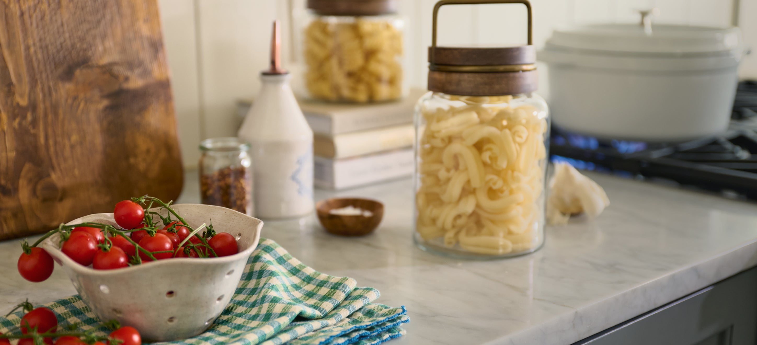 Kitchen counter with tomatoes, pasta, and a jar on a checkered towel
