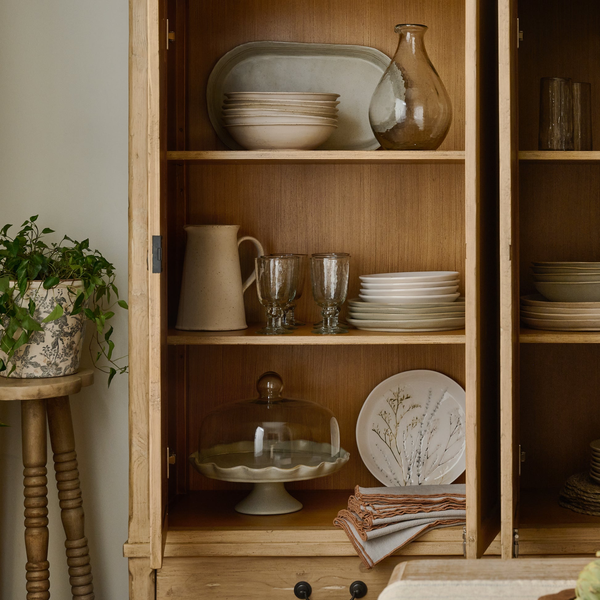 Hurston Wide Cabinet in aged light pine with doors open and plates and glass cups stored inside