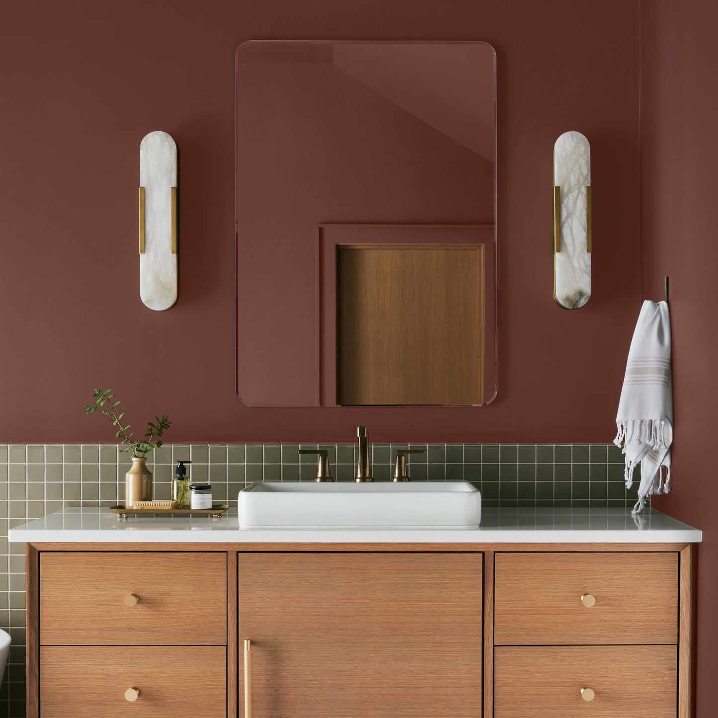 Mountain Currant paint featured in bathroom walls with marble sconces and light wood cabinetry and white sink