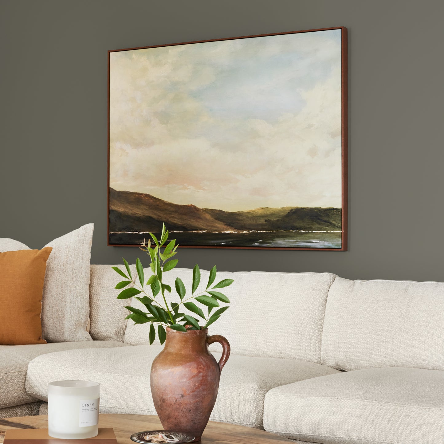 Trailhead paint featured in living room walls with large landscape picture above cream sectional and brown vase and greenery