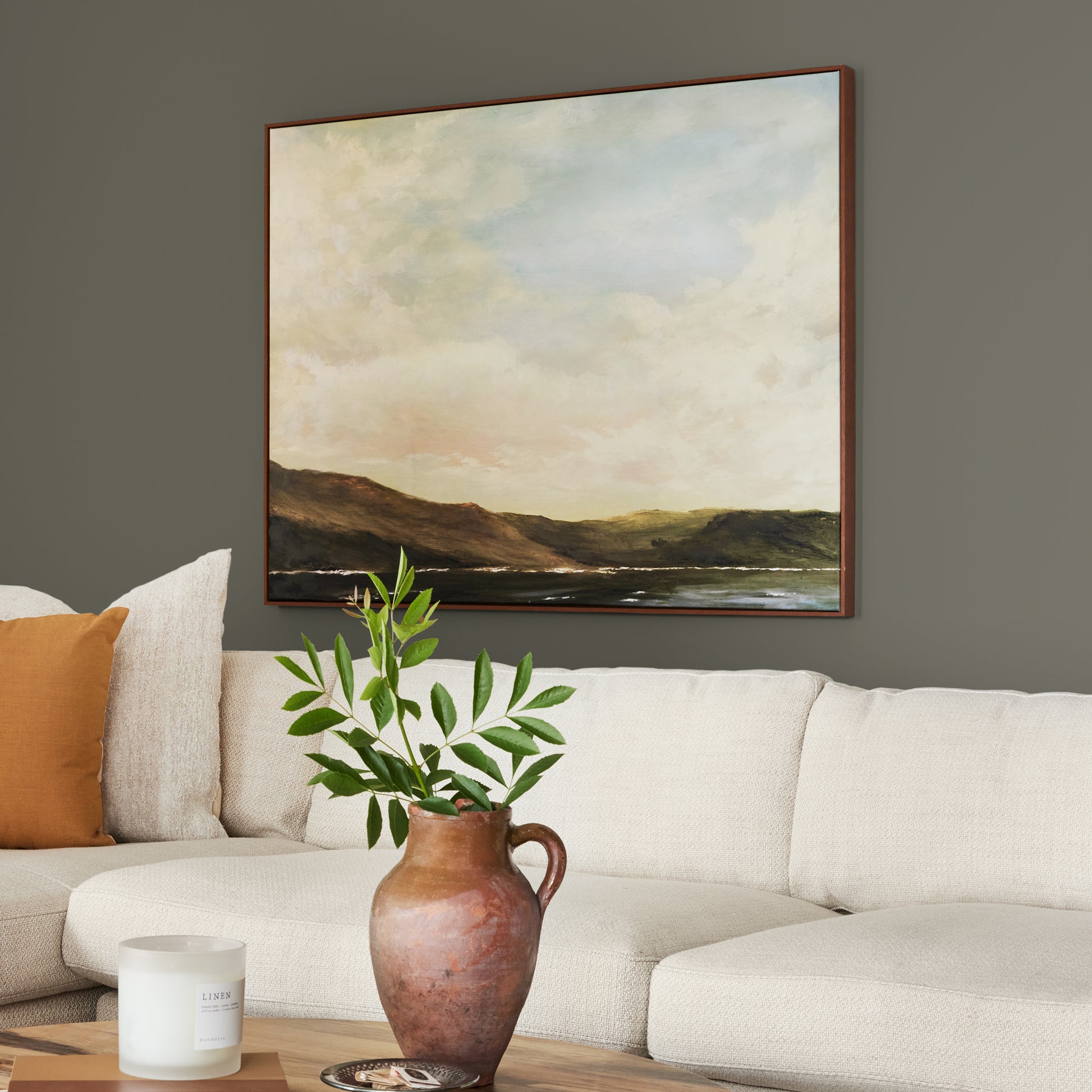 Trailhead paint featured in living room walls with large landscape picture above cream sectional and brown vase and greenery