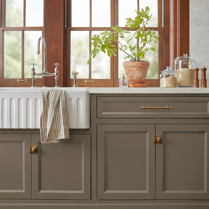 Mosswood paint featured on bottom kitchen cabinetry with farmhouse sink, glass storage and potted plant