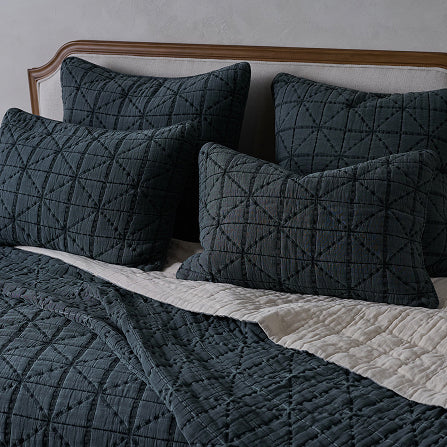 Dark gray quilt and pillow set on a bed with a wooden headboard.  Shop blue bedding.