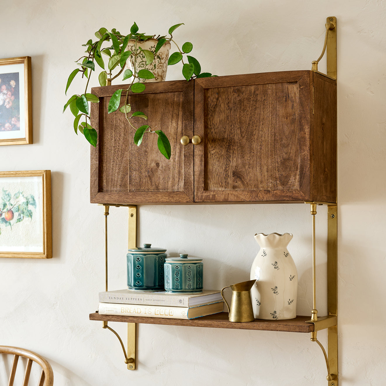 Wooden wall-mounted cabinet with brass accents, shelves, and decorative items on a light-colored wall.