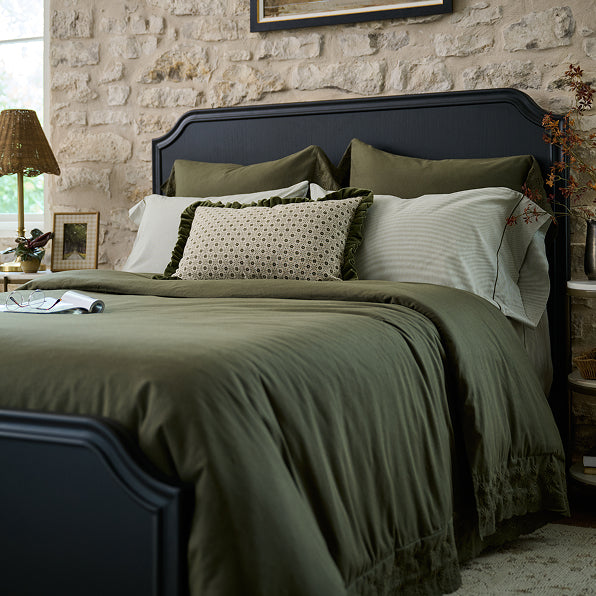 Bedroom with a bed featuring green bedding and pillows against a stone wall.