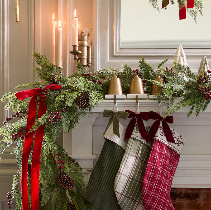 three stockings hung from a white holiday mantel decorated with green garland and red berries.