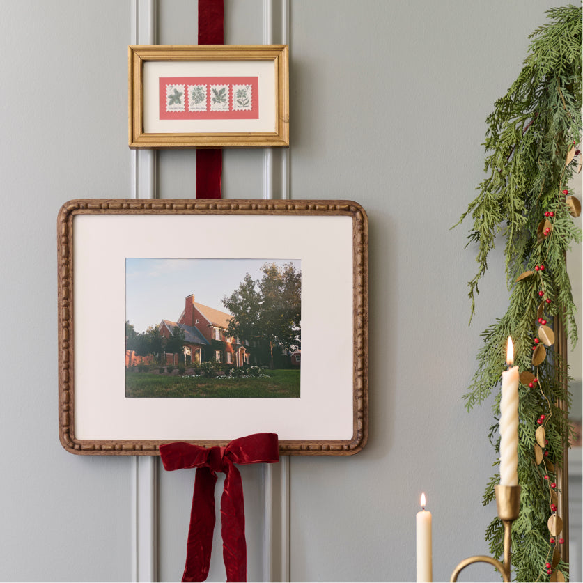 Framed picture with a red ribbon on a wall with Christmas decorations.