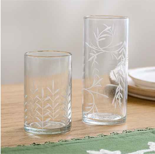 Two clear glass tumblers with floral etching on a wooden surface.