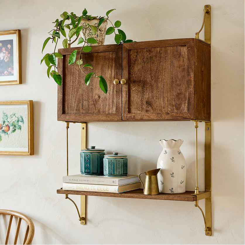 Wooden wall-mounted cabinet with brass accents, shelves, and decorative items against a light wall.