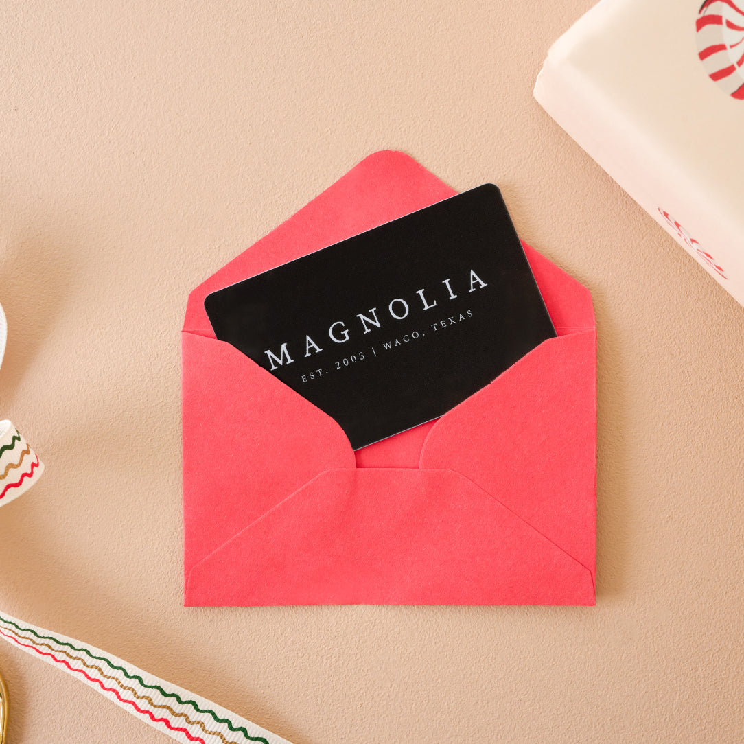 Black card with 'MAGNOLIA' branding in a pink envelope on a beige surface.