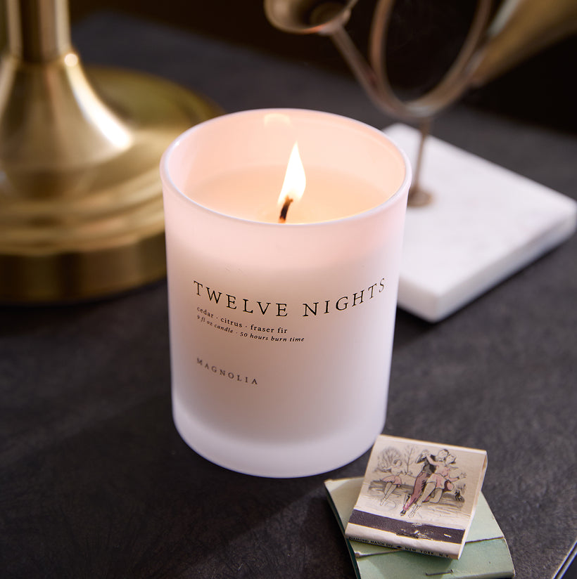 Candle labeled 'Twelve Nights' on a dark surface with decorative elements.