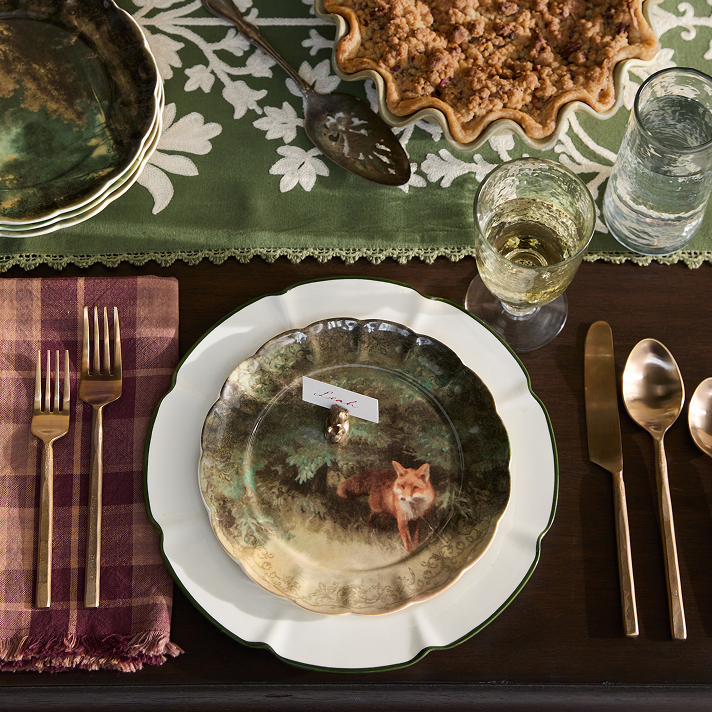 Dining table setting with a decorative plate featuring a fox design, glasses, and cutlery.