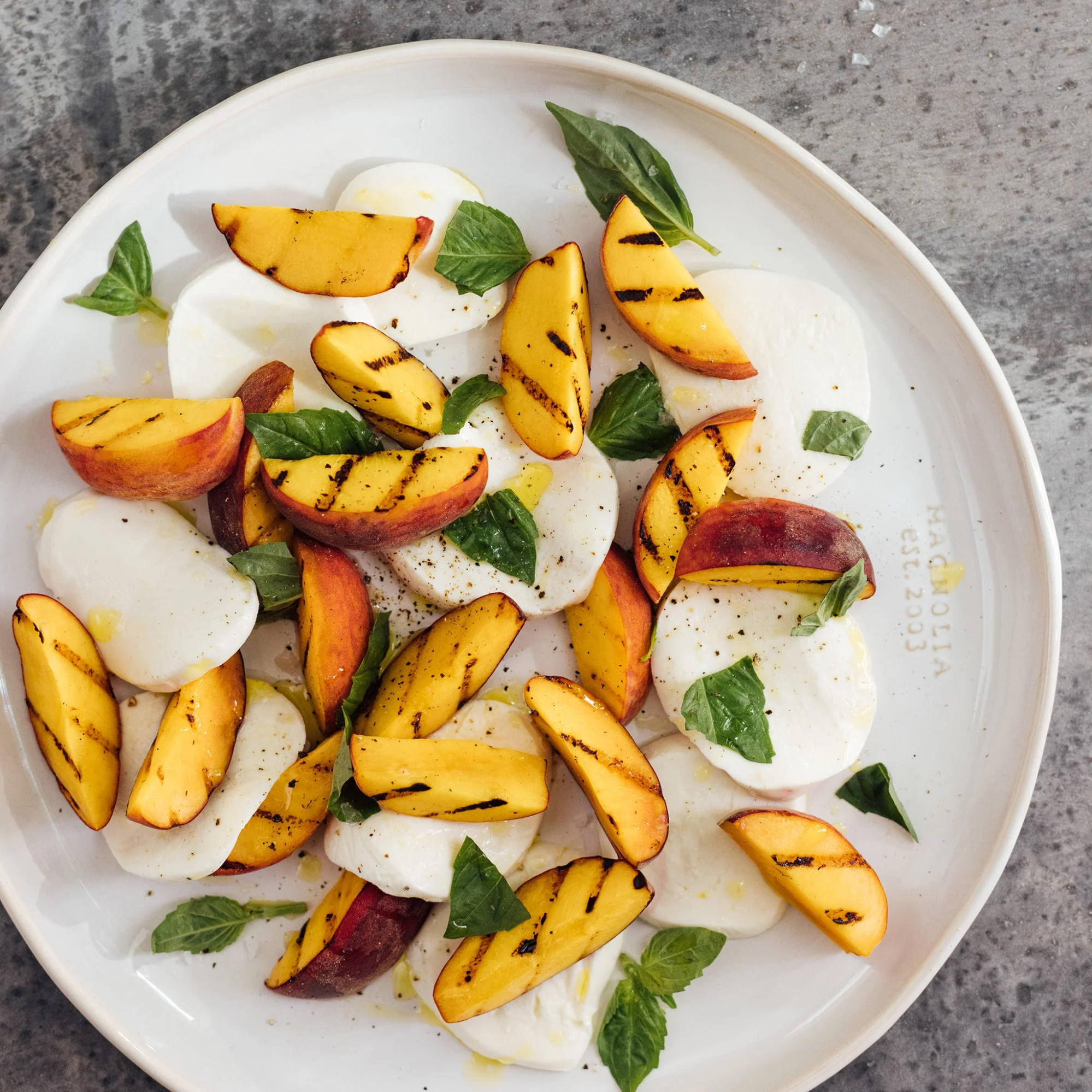 Platter of grilled peach and mozzarella salad on a gray surface