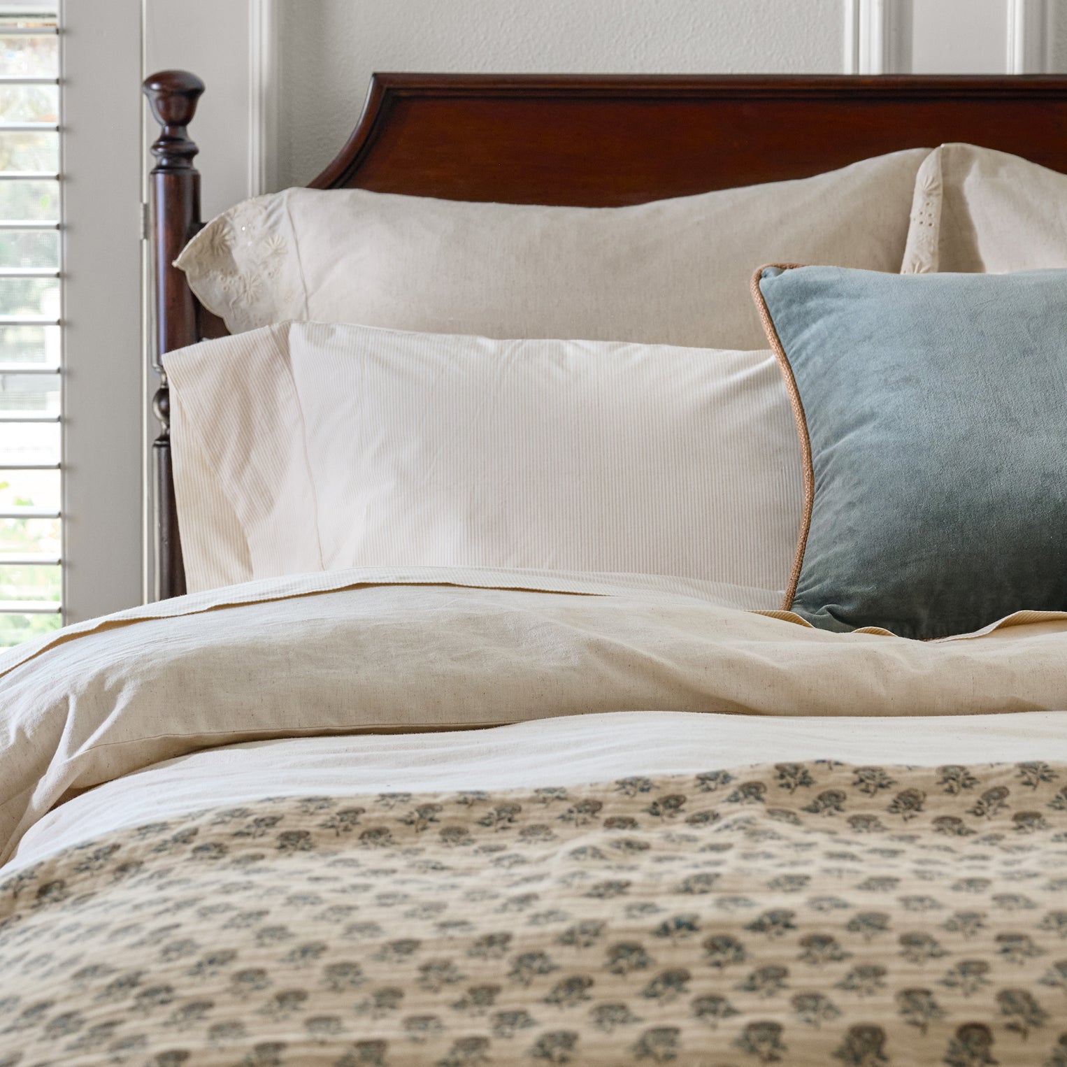 Brown headboard with two bed pillows in neutral bedding.  There is a blue throw pillow on top.  The bedding is a neutral with a blue pattern.